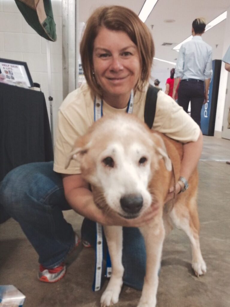 Woman holding a white dog with brown spots.